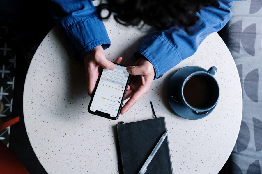 Personne lisant un message sur son smartphone à une table, avec une tasse et un carnet