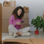 Une jeune femme consulte son téléphone entourée de cartons