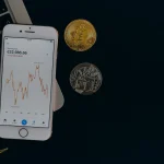 Un smartphone affichant un cours de cryptomonnaie posé sur un ordinateur portable